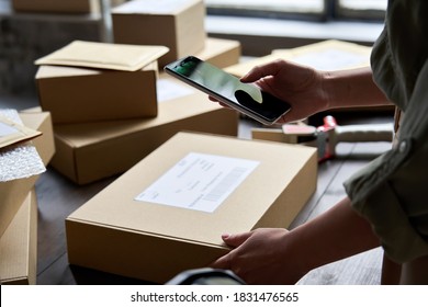 Female Warehouse Worker Seller, Small Stock Business Owner Holding Phone Scanning Retail Package Parcel Bar Code On Commercial Shipping Box Delivery Order On Smartphone Using Mobile App.