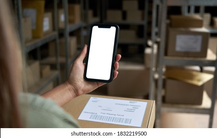 Female Warehouse Worker Seller, Small Stock Business Owner Holding Phone Mock Up Screen Ad Scan Retail Package Parcel Bar Code On Commercial Shipping Box Delivery Order On Smartphone Using Mobile App.