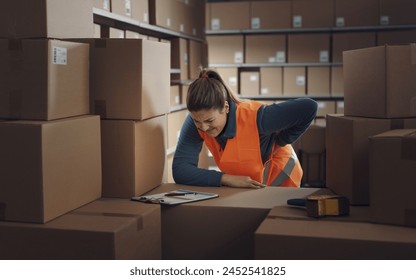 Female warehouse worker touching her lower back, she is having back pain - Powered by Shutterstock