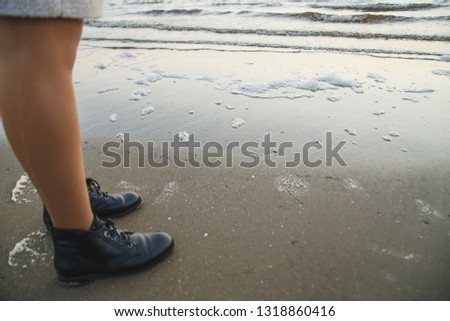 Female in waterproof leather boots on sea sand.