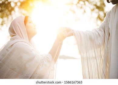 A female wearing a biblical robe and grabbing the hand of Jesus Christ for help and guidance