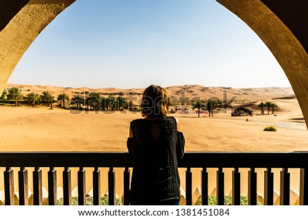 A female wearing black clothes looking out into the dunes in a desert during sunset