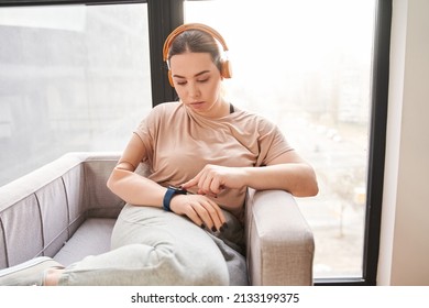 Female Wearing Headphones With Arm Implant Sitting At The Armchair And Touching To The Smartwatch