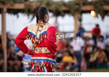 A female wearing a red jingle dress with colorful beads.