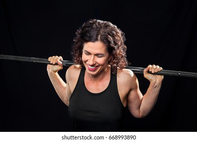 A Female Weight Lifter, Holding A Barbell On Her Shoulders, Laughs With Eyes Closed.  She Looks Like She Is Pushing Through A Hard Set Of Back Squats.