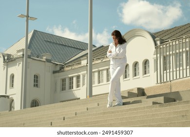 Female in white tracksuit, descending steps in front of a modern white building, exuding confidence. Concept: Highlighting the synergy between contemporary urban environments and personal fitness - Powered by Shutterstock