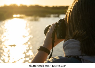 Female Wildlife Photographer Captures With Her Camera The Sunset Over A River In The African Wilderness, Photographed From Behind