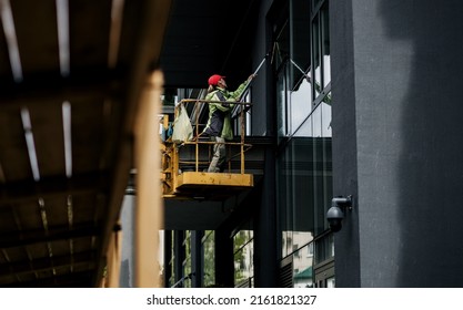 Female Window Cleaner Cleaning Glass Windows On Modern Building High In The Air On A Lift Platform. 