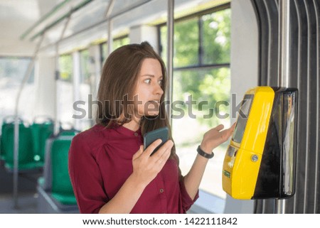 Female Woman paying conctactless with smartphone for the public transport in the tram. Yellow ticket machine in the modern tram