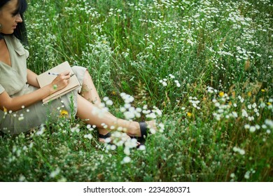 Female woman with pen writing or painting, handwriting on notebook on flower blooming meadow, in countryside outdoor, in the field on summer day in meadow, feel the nature, relax, alone travel. - Powered by Shutterstock