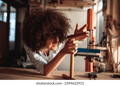 Female Woodworker Inspecting Handcrafted Piece in Sunlit Workshop - Powered by Shutterstock