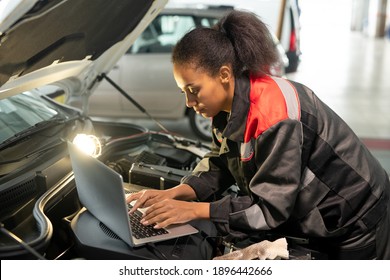 Female Worker Of Car Maintenance Service Bending Over Open Engine Compartment While Using Laptop To Look For Data In Online Sources