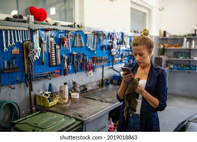 Female worker of car repair service in uniform using laptop and smartphone in workshop to look for data in online sources, take new orders or consult clients. Female mechanic relaxing using mobile - Powered by Shutterstock