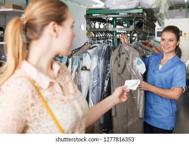 Female Worker Of Dry Cleaner Returning Clean Clothes To Customer On Reception