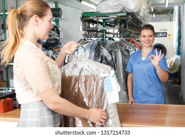 Female Worker Of Dry Cleaner Returning Clean Clothes To Customer On Reception
