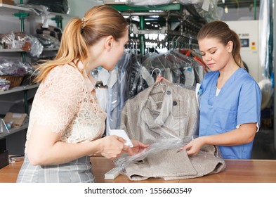 Female Worker Of Dry Cleaner Returning Clean Clothes To Customer On Reception
