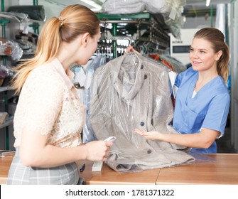 Female Worker Of Dry Cleaner Returning Clean Clothes To Customer On Reception
