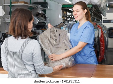 Female Worker Of Dry Cleaner Returning Clean Clothes To Customer On Reception
