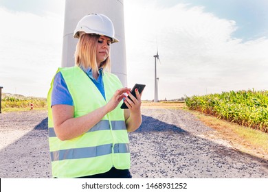 Female Worker Engineer Speaking On The Mobile Phone Outdoors In Field Of A Wind Power Turbines. Female Employment And Renewable Energy Concept