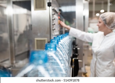 Female worker in factory checking robotic line for water bottling and packing. Inspection of quality control. Selective focus.