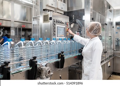 Female worker in factory checking robotic line for water bottling and packing. Inspection of quality control. Selective focus.
