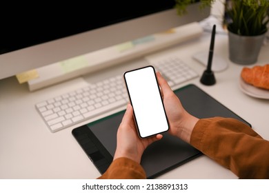 Female worker or graphic designer chatting with her friends, reading an information on the website, using her smartphone over her modern office desk. - Powered by Shutterstock