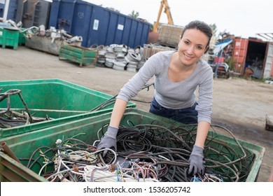 female worker holding cables in a scrap recycling yard - Powered by Shutterstock