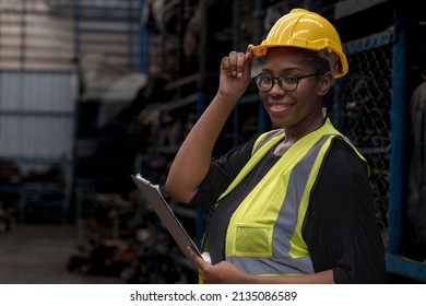 Female worker holding a hat and looking at the camera. Engineers or technicians are inspecting auto parts in warehouses and factories. African American woman holding a flip chart in parts warehouse.