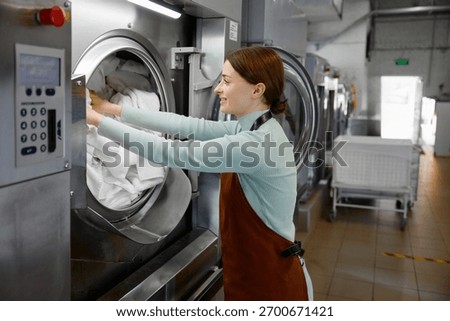 Female worker is loading various clothes into a washing machine