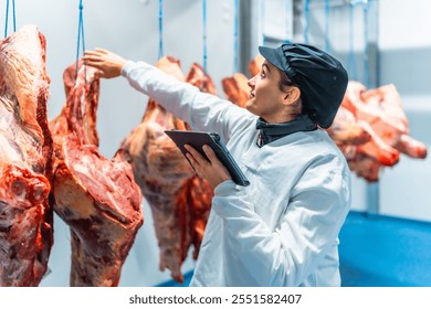 Female worker in meat factory using a wifi tablet to check and record the quality of the products - Powered by Shutterstock