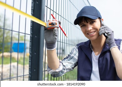 female worker on telephone measuring a metal fence