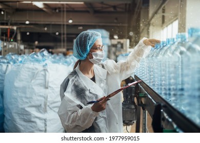 Female Worker With Protective Face Mask Working In Medical Supplies Research And Production Factory And Checking Canisters Of Distilled Water Before Shipment. Inspection Quality Control. 