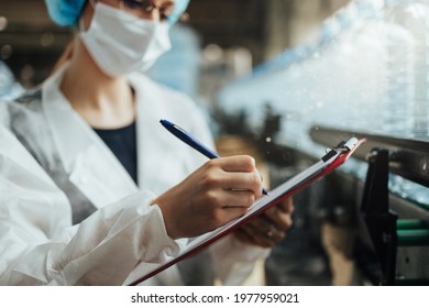 Female Worker With Protective Face Mask Working In Medical Supplies Research And Production Factory And Checking Canisters Of Distilled Water Before Shipment. Inspection Quality Control. 