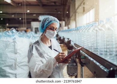 Female Worker With Protective Face Mask Working In Medical Supplies Research And Production Factory And Checking Canisters Of Distilled Water Before Shipment. Inspection Quality Control. 