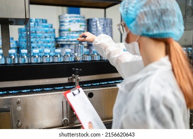 Female Worker With Protective Face Mask Working In Medical Supplies Research And Production Factory And Checking Canisters Of Distilled Water Before Shipment. Inspection Quality Control.