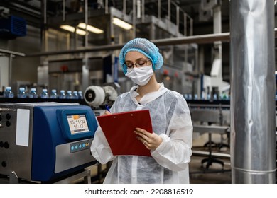 Female Worker With Protective Face Mask Working In Medical Supplies Research And Production Factory And Checking Canisters Of Distilled Water Before Shipment. Inspection Quality Control. 