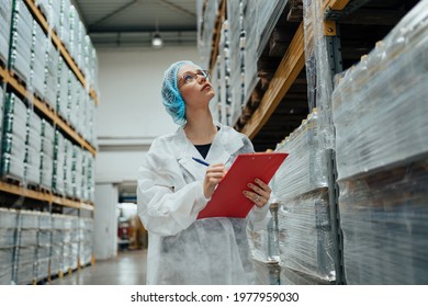 Female Worker In Protective Workwear Working In Medical Supplies Research And Production Factory And Checking Packed Canisters Of Distilled Water Before Shipment. Industrial Warehouse.