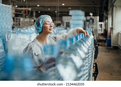 Female Worker In Protective Workwear Working In Medical Supplies Research And Production Factory And Checking Canisters Of Distilled Water Before Shipment. Inspection Quality Control. 