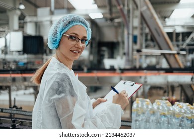 Female Worker In Protective Workwear Working In Medical Supplies Research And Production Factory And Checking Canisters Of Distilled Water Before Shipment. Inspection Quality Control. 