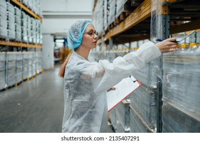 Female Worker In Protective Workwear Working In Medical Supplies Research And Production Factory And Checking Packed Canisters Of Distilled Water Before Shipment. Industrial Warehouse.