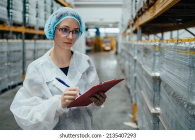 Female Worker In Protective Workwear Working In Medical Supplies Research And Production Factory And Checking Packed Canisters Of Distilled Water Before Shipment. Industrial Warehouse.