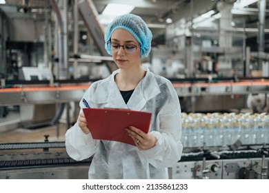 Female Worker In Protective Workwear Working In Medical Supplies Research And Production Factory And Checking Canisters Of Distilled Water Before Shipment. Inspection Quality Control.