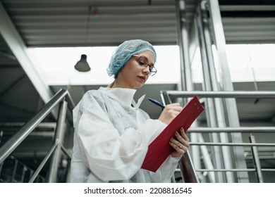 Female Worker In Protective Workwear Working In Medical Supplies Research And Production Factory And Checking Canisters Of Distilled Water Before Shipment. Inspection Quality Control. 