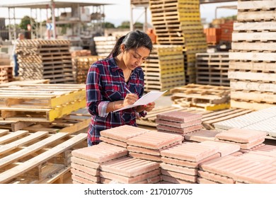 Female worker with tablet checking quantity of paving slabs in warehouse of building materials