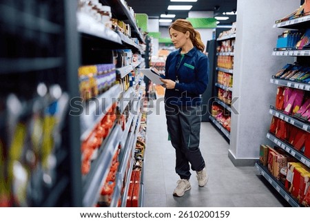 Female worker taking notes while checking stock of shelves at supermarket. 