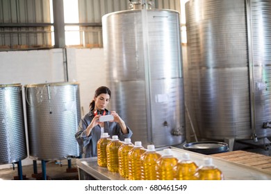 Female worker taking photo of oil bottles from mobile phone in oil factory - Powered by Shutterstock