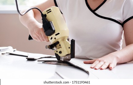 Female worker uses electric cutting fabric machine. Fabric industry production