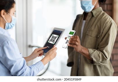 Female Worker Using App On Digital Tablet, Scanning Health QR Code Of Black Male Visitor On Entrance To Public Place, African American Man Demonstrating Vaccination Certificate On Smartphone, Closeup - Shutterstock ID 2045195849