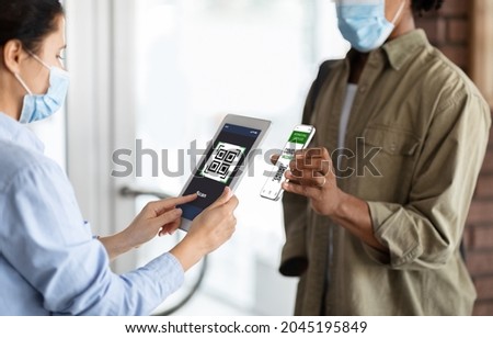 Female Worker Using App On Digital Tablet, Scanning Health QR Code Of Black Male Visitor On Entrance To Public Place, African American Man Demonstrating Vaccination Certificate On Smartphone, Closeup