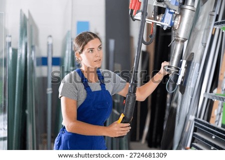 Female worker using control panel and lifting mechanism controls the movement of window panes in an industrial workshop